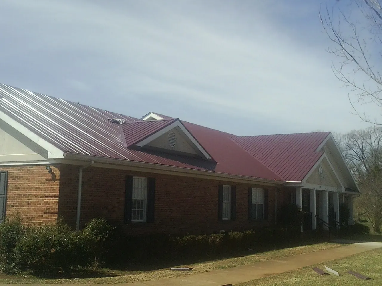 Red metal roof with gabled entries on a long brick building, from a Hail Damage Roof Repair job in Mobile