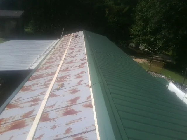 Old rusted panels beside newly installed green metal roofing — Wind Damage Roof Repair by Roofing Brothers in Mobile