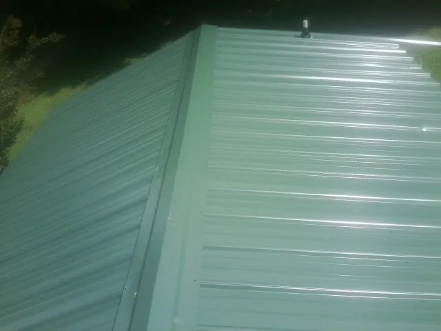 New green metal panels meeting at the ridge of a roof — Flat Roof Repair work by our crew in Mobile