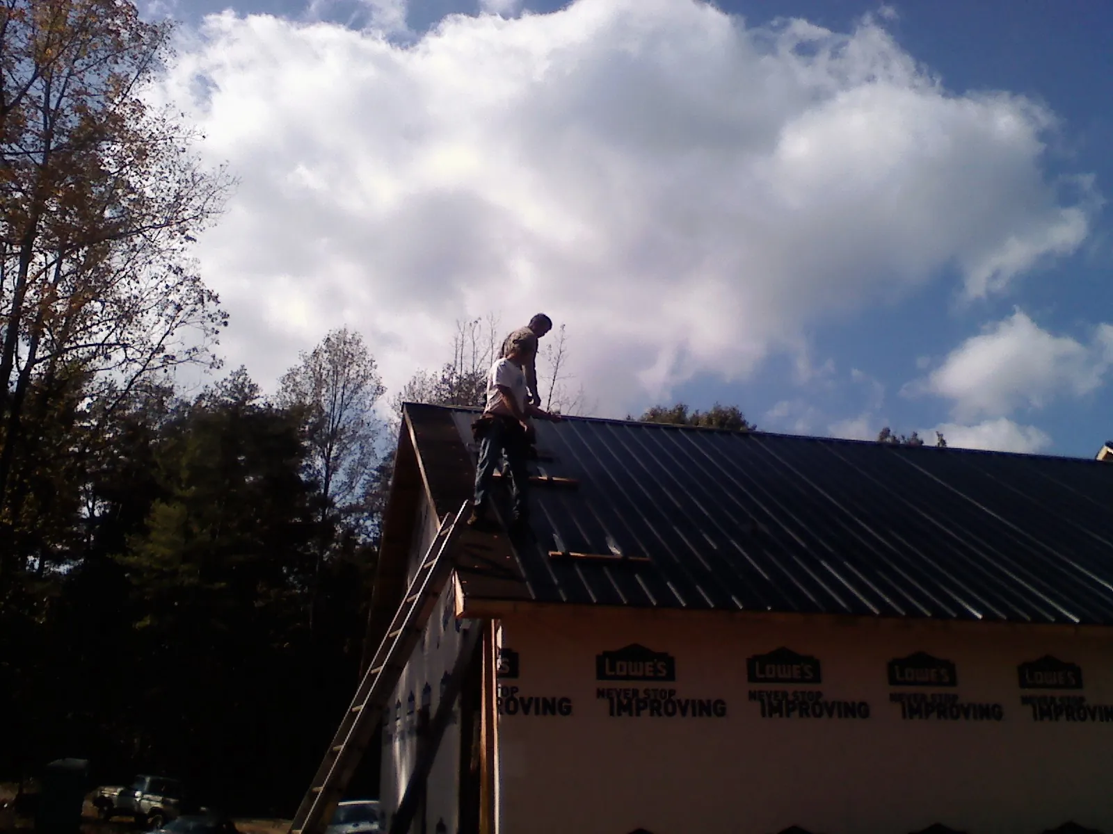 Roofer fastening dark metal panels high against a cloudy sky, from a Roof Inspection job in Mobile